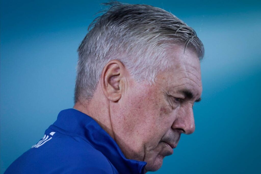 Carlo Ancelotti in primo piano durante un impegno stampa del 2024, con lo sguardo rivolto verso il basso.