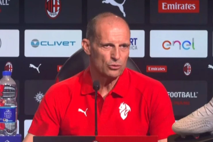 Massimiliano Allegri durante una conferenza stampa al Milan con microfono davanti a uno sfondo con loghi di sponsor
