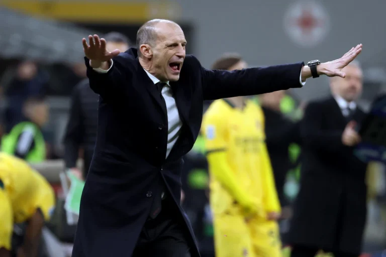 Massimiliano Allegri allena il Milan dalla panchina durante una partita, con le braccia aperte in gesto di comunicazione verso i giocatori
