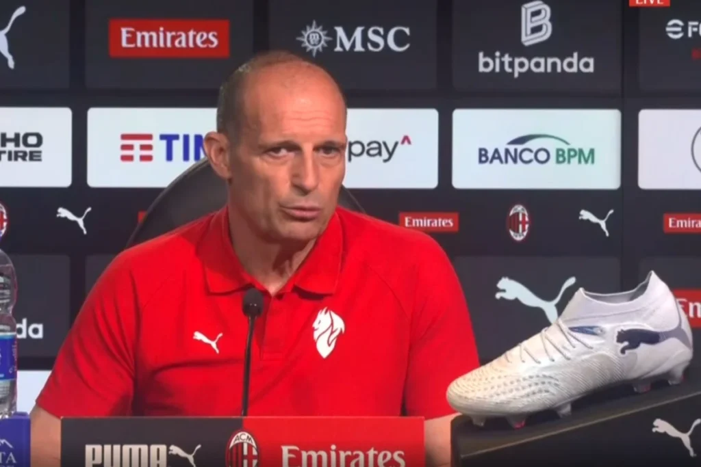 Massimiliano Allegri in conferenza stampa con microfono, indossa polo rossa Puma del Milan