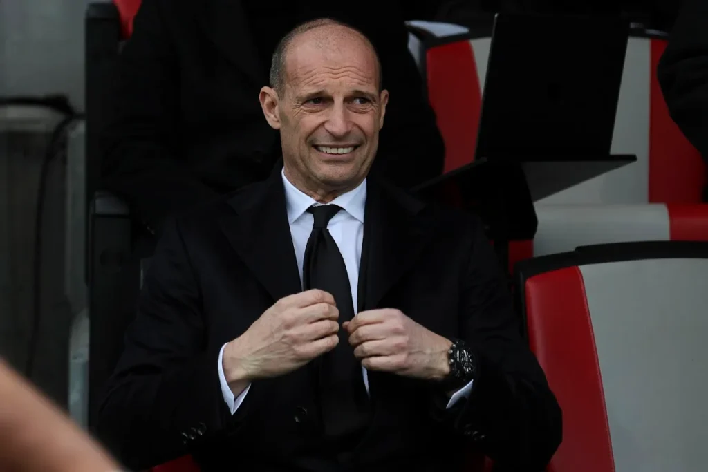 Massimiliano Allegri sorride in panchina durante una partita, indossa completo nero e cravatta nera