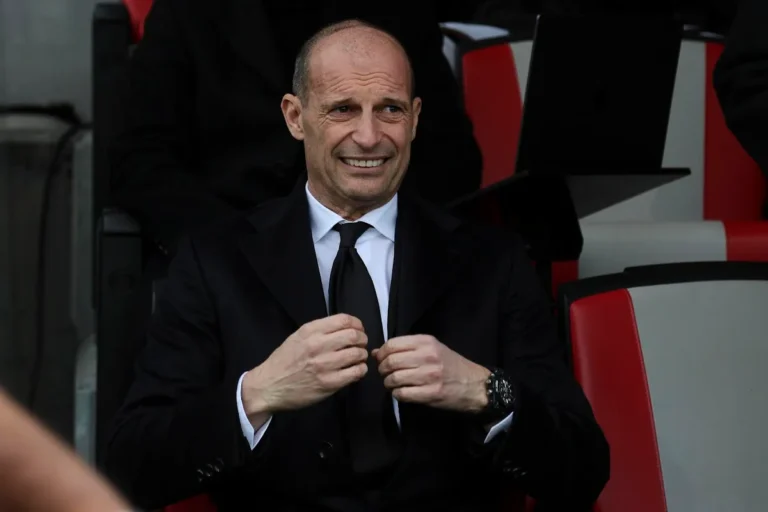 Massimiliano Allegri sorride in panchina durante una partita, indossa completo nero e cravatta nera