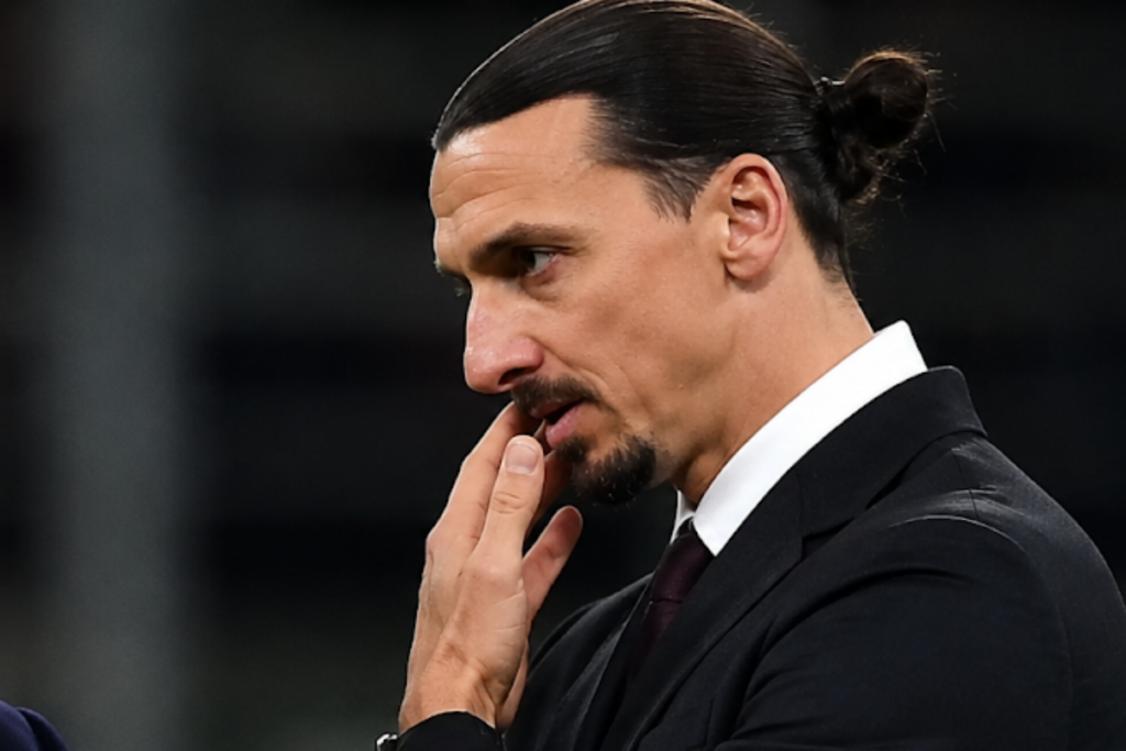 Zlatan Ibrahimovic in abito nero con cravatta, espressione pensierosa, mano al viso in concentrazione