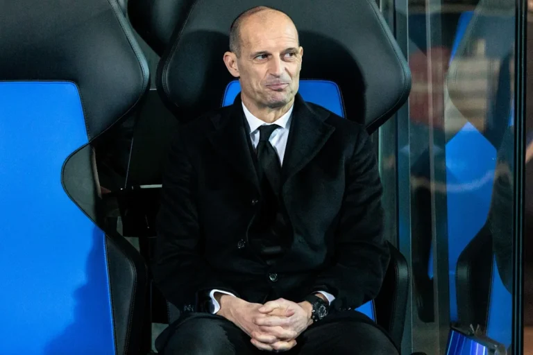 Massimiliano Allegri seduto in panchina, indossa abito nero e cravatta, osserva la partita con concentrazione