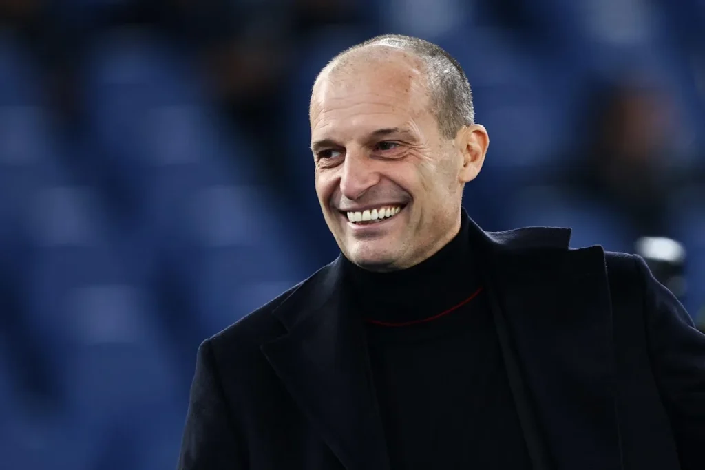 Massimiliano Allegri sorride durante un evento calcistico, indossando un cappotto nero