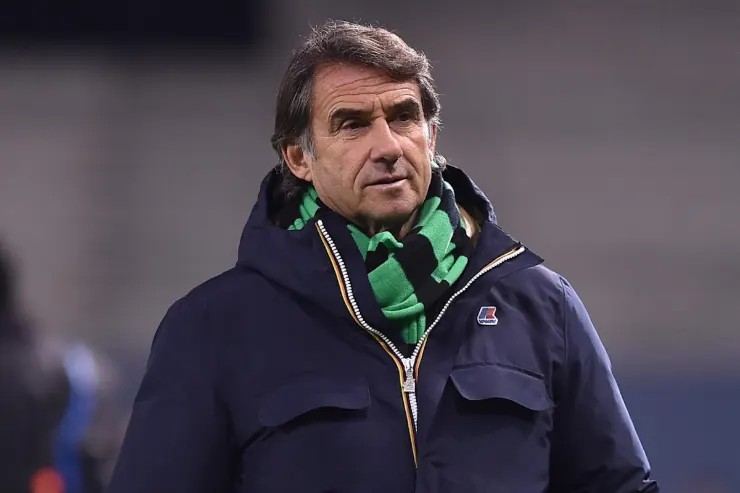 Giovanni Carnevali in giacca blu e sciarpa verde durante una partita, osservando il campo