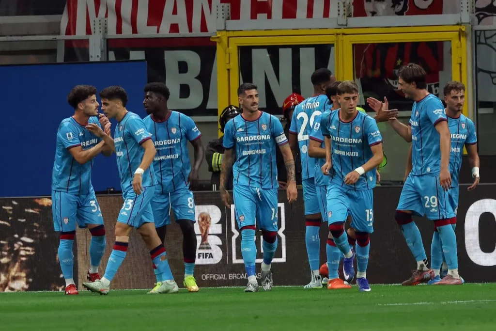 Giocatori del Cagliari in maglia azzurra durante la partita contro il Milan, con celebrazione in panchina