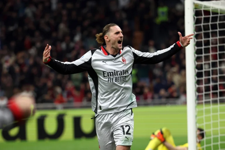 Adrien Rabiot in maglia bianca del Milan con braccia aperte durante una partita, accanto al palo della porta