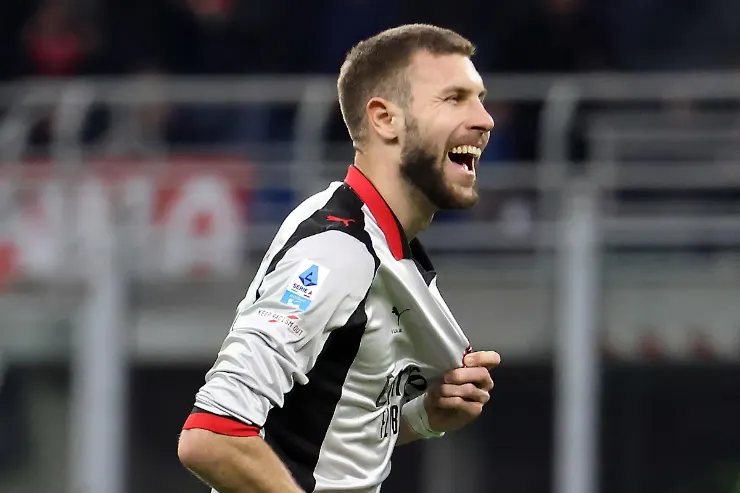 Pavlovic sorride durante una partita del Milan, indossa la maglia rossonera con dettagli bianchi e neri