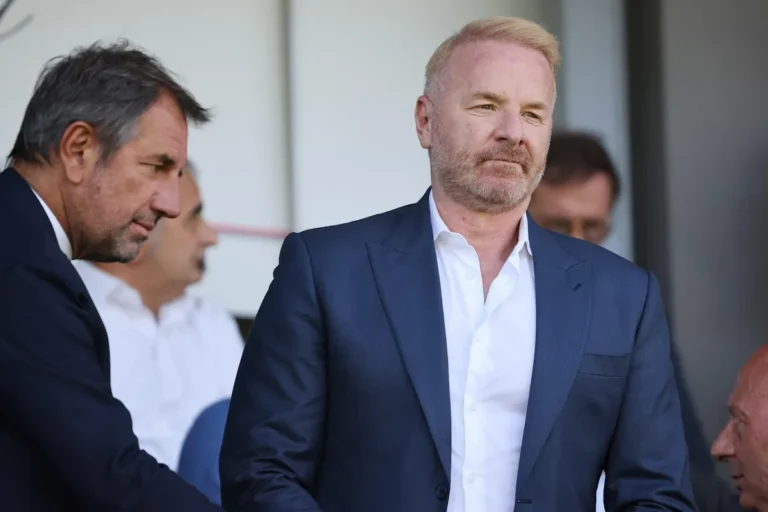 Igli Tare in abito blu scuro con camicia bianca durante un evento ufficiale, ritratto in primo piano accanto ad altri dirigenti