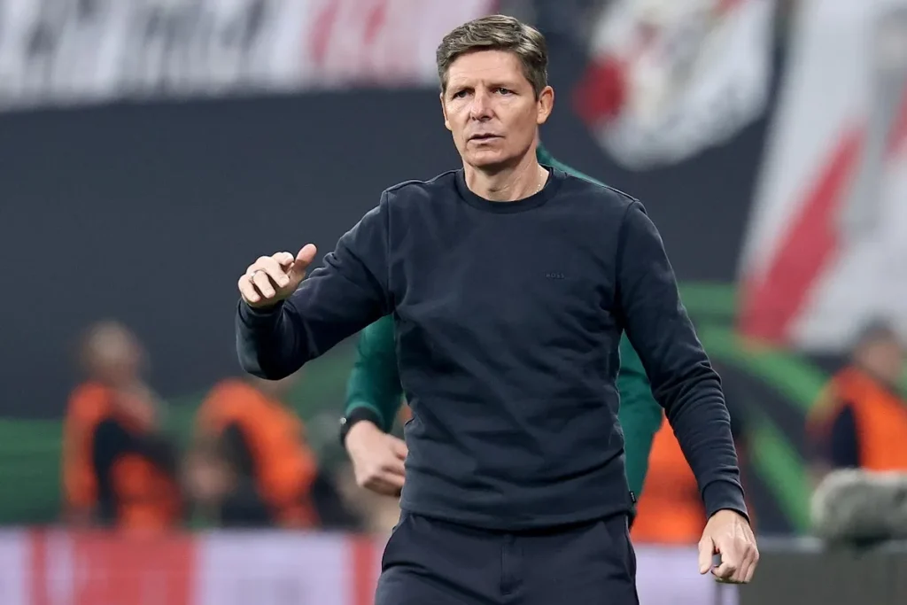 Oliver Glasner in tuta nera sul campo durante una partita, con lo staff tecnico sullo sfondo