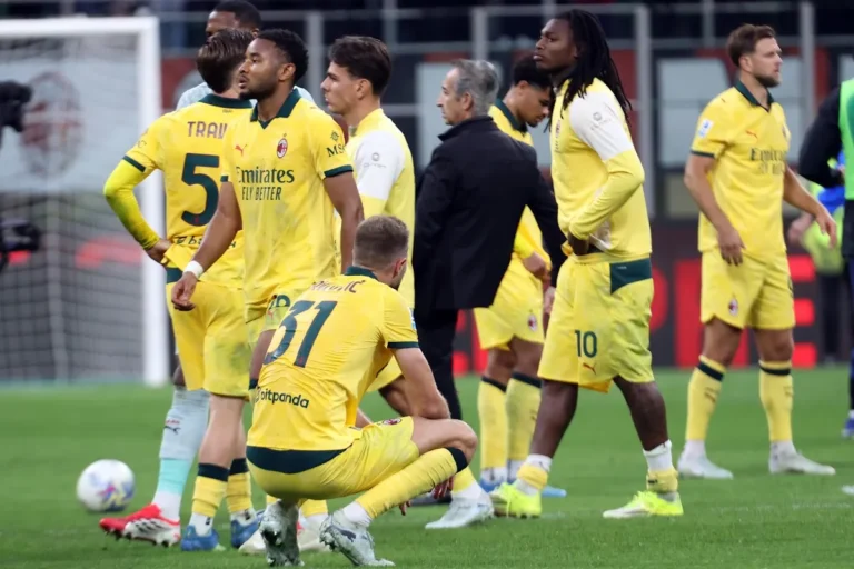 Calciatori del Milan in maglia gialla riuniti in campo, alcuni in atteggiamento pensieroso durante una pausa di gioco