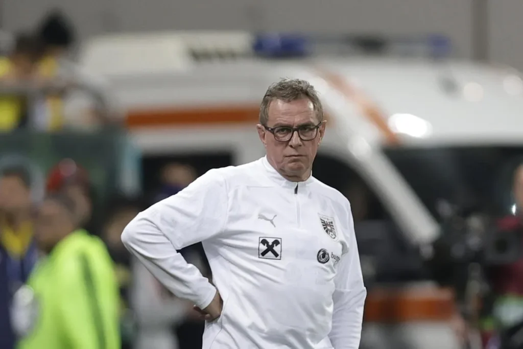 Ralf Rangnick in tuta bianca ufficiale durante una partita, con le mani sui fianchi in panchina