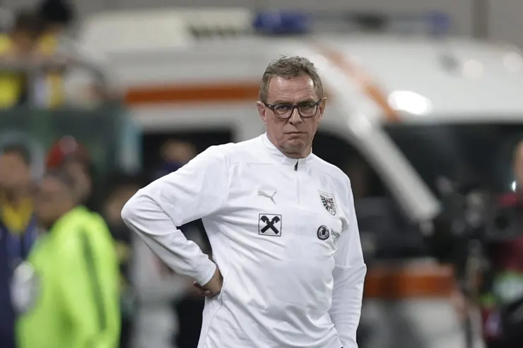 Rangnick in tuta tecnica bianca durante una partita, con le mani sui fianchi in panchina