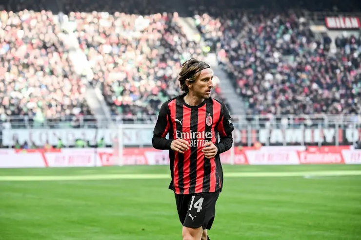 Luka Modrić in maglia rossonera número 14 durante una partita al Meazza con gli spalti pieni sullo sfondo