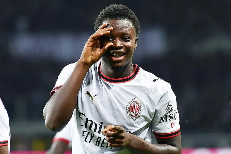 Giocatore del Milan in maglia bianca sorride durante la partita, indossa la divisa Puma con logo rossonero