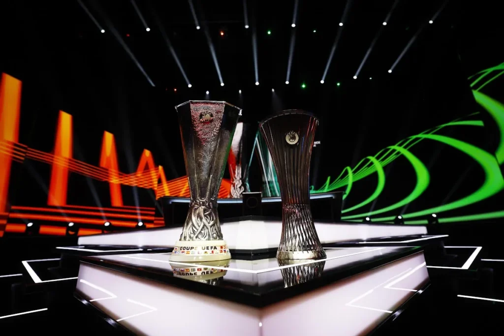 Trofei della UEFA Europa League e Conference League esposti su un palco illuminato durante il sorteggio