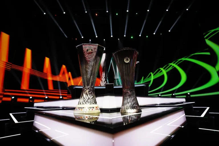 Trofei della UEFA Europa League e Conference League esposti su un palco illuminato durante il sorteggio