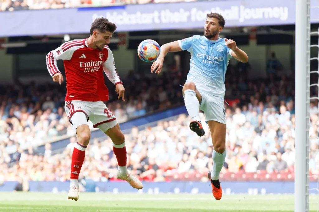 Giocatore dell'Arsenal in maglia rossa e difensore del Manchester City in celeste contendono la palla in salto durante la FA Community Shield
