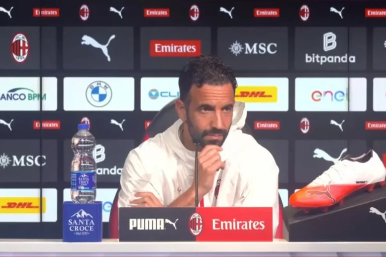 Ruben Amorim durante una conferenza stampa con microfono, in posizione pensierosa, con sponsor Milan sullo sfondo