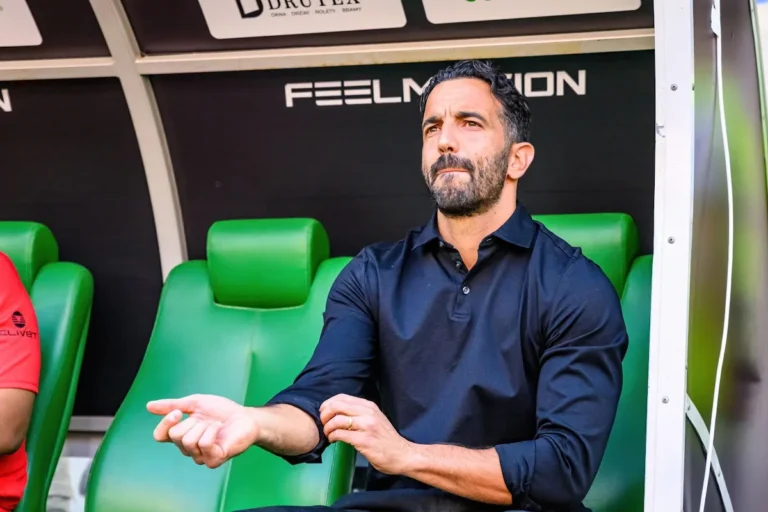 Allenatore in panchina con espressione concentrata, seduto sui seggiolini verdi dello stadio durante una partita di Serie A