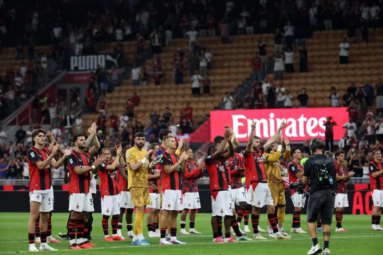 Giocatori del Milan in divisa rossonera applaudono i tifosi dopo la partita, con lo stadio pieno sullo sfondo