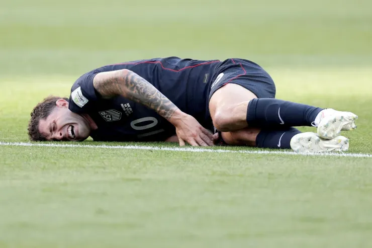 Pulisic a terra sul campo di gioco durante una partita, indossa la maglia scura della nazionale USA