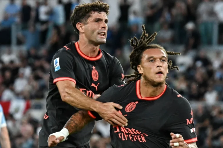 Pulisic e Moreira in maglia Milan nera con dettagli rossi celebrano durante una partita, con lo stemma rossonero visibile