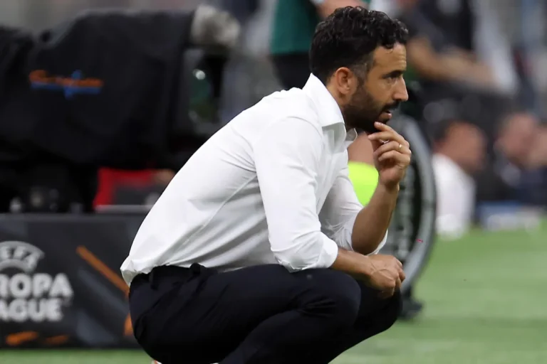 Amorim accovacciato a bordo campo con camicia bianca e mano sul mento, pannello UEFA Europa League alle spalle