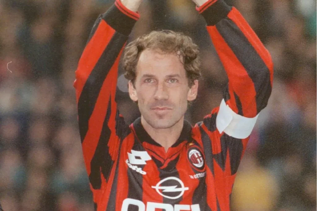 Giocatore del Milan con maglia rossonera a strisce e fascia da capitano bianca, braccia alzate verso il pubblico