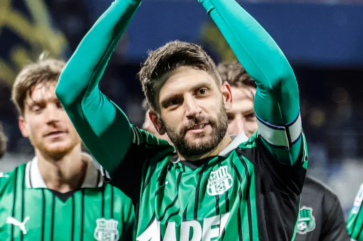 Giocatore del Sassuolo in maglia verde a righe nere esulta con le braccia alzate durante una partita