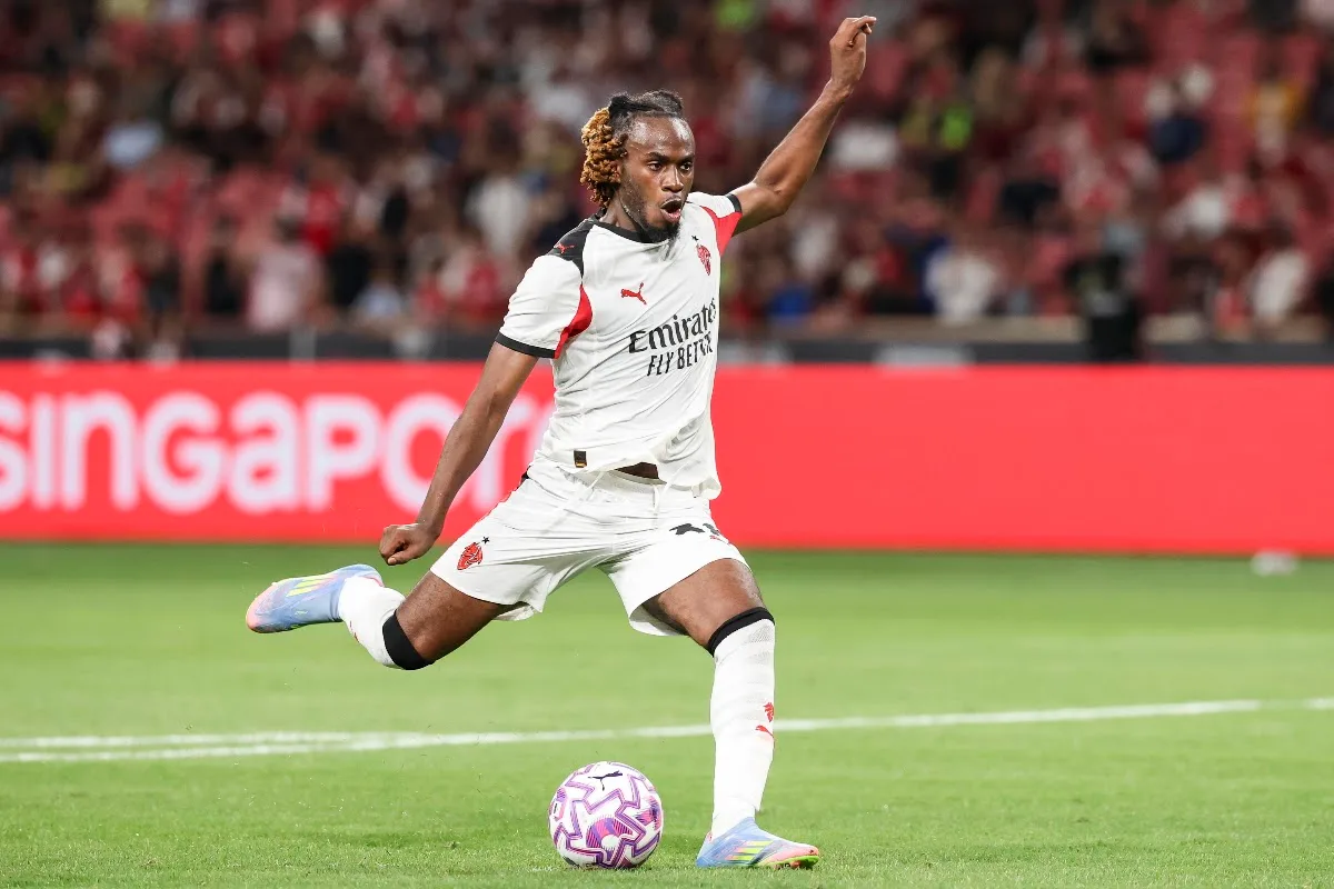 Bondo in campo con la maglia bianca del Milan mentre calcia il pallone, con sponsor Emirates e tifosi sullo sfondo