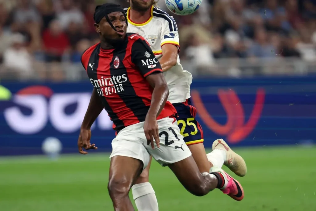 Chukwueze con la maglia rossonera a righe durante una partita del Milan, contrasto con un avversario in maglia bianca