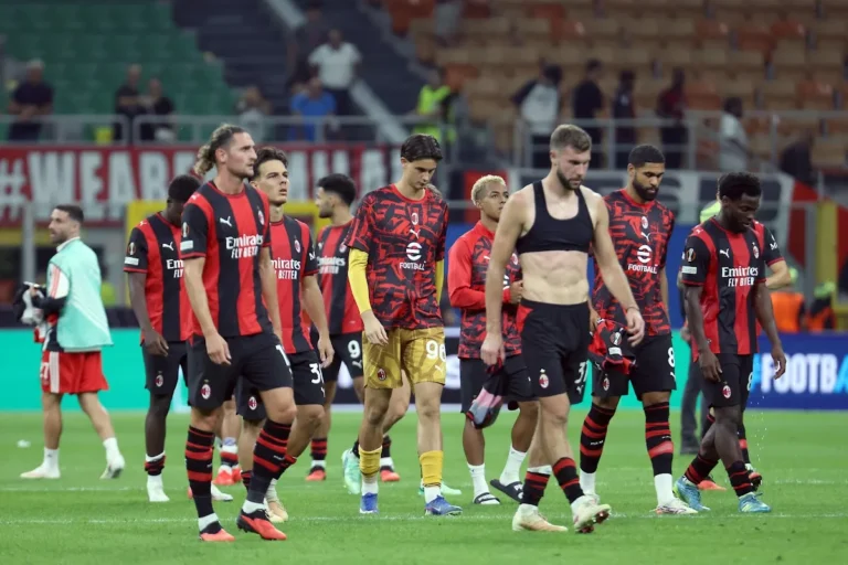 Giocatori del Milan con maglia rossonera a testa bassa dopo la partita, camminano sul prato di San Siro