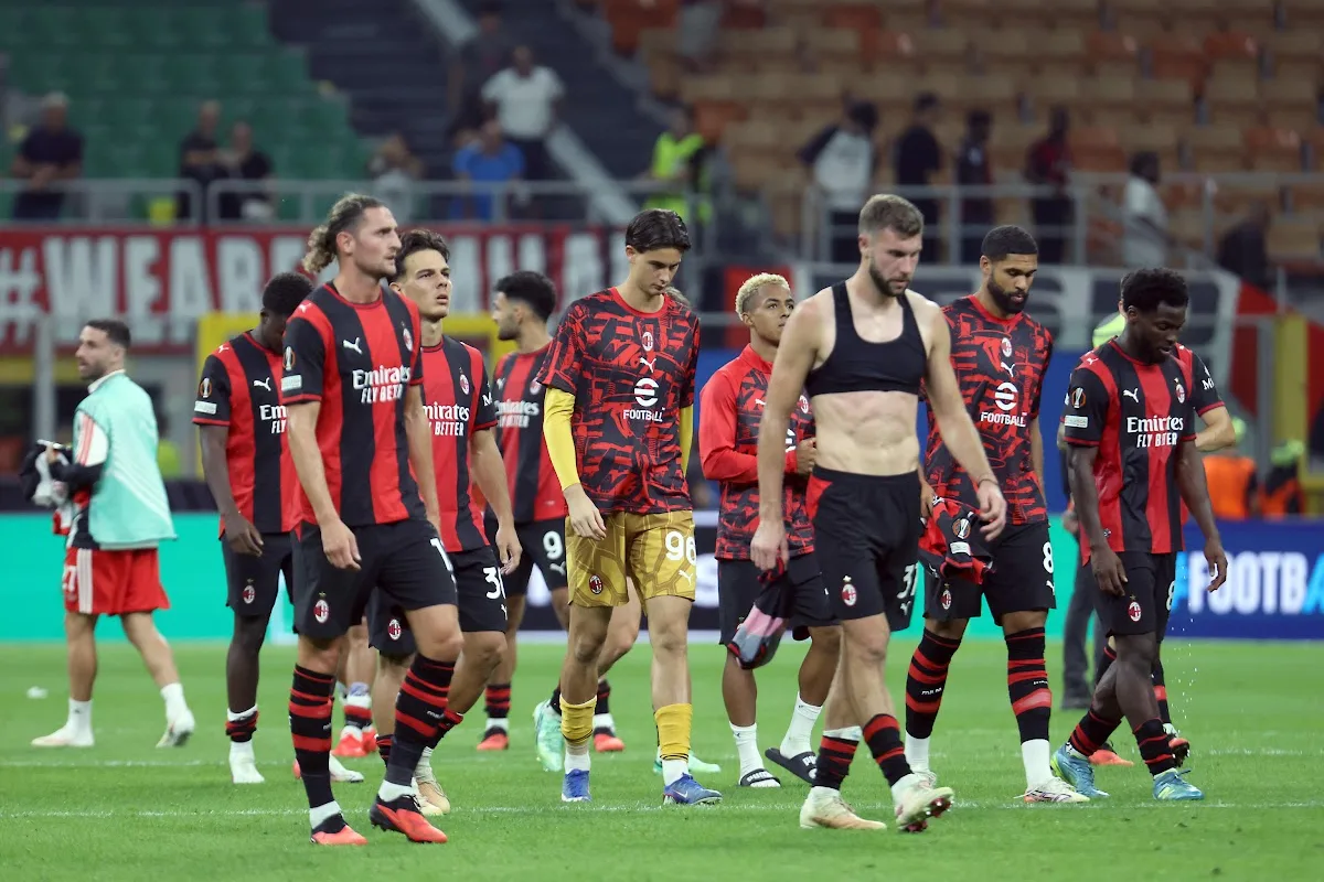 Giocatori del Milan con maglia rossonera a testa bassa dopo la partita, camminano sul prato di San Siro