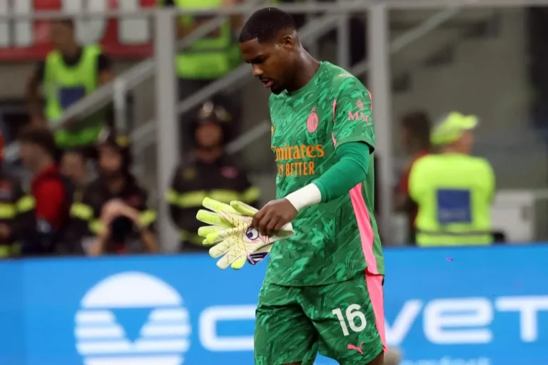 Mike Maignan, portiere del Milan con maglia verde e numero 16, guanti gialli in mano, a testa bassa durante una partita