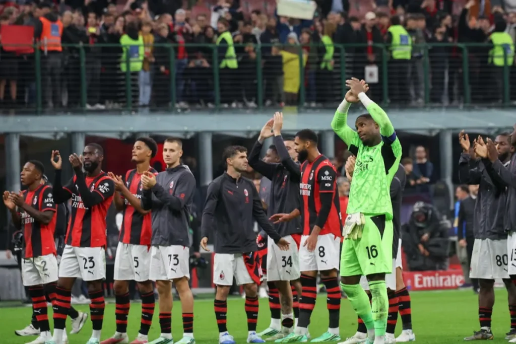 Giocatori del Milan salutano i tifosi sotto la curva al termine di una partita in casa, con la maglia rossonera a strisce