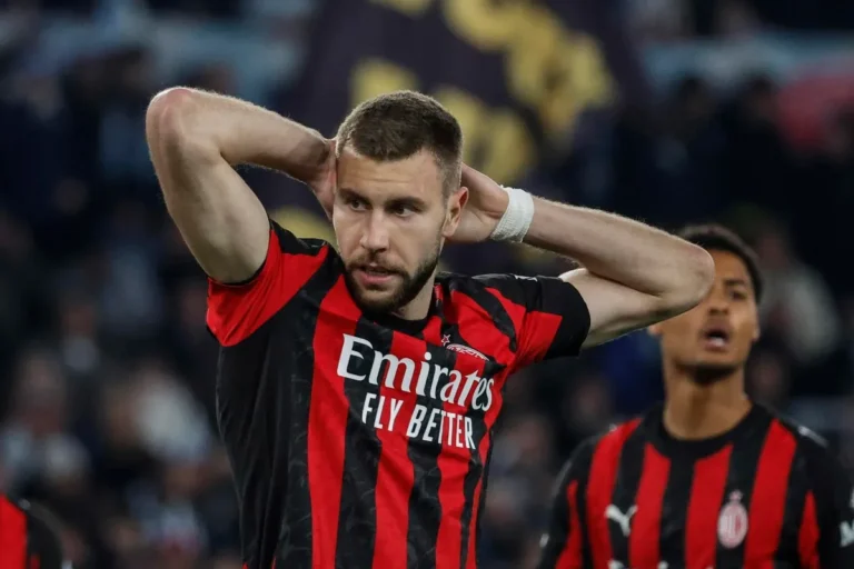 Difensore del Milan con maglia rossonera Emirates, mani sulla testa e sguardo deluso durante una partita