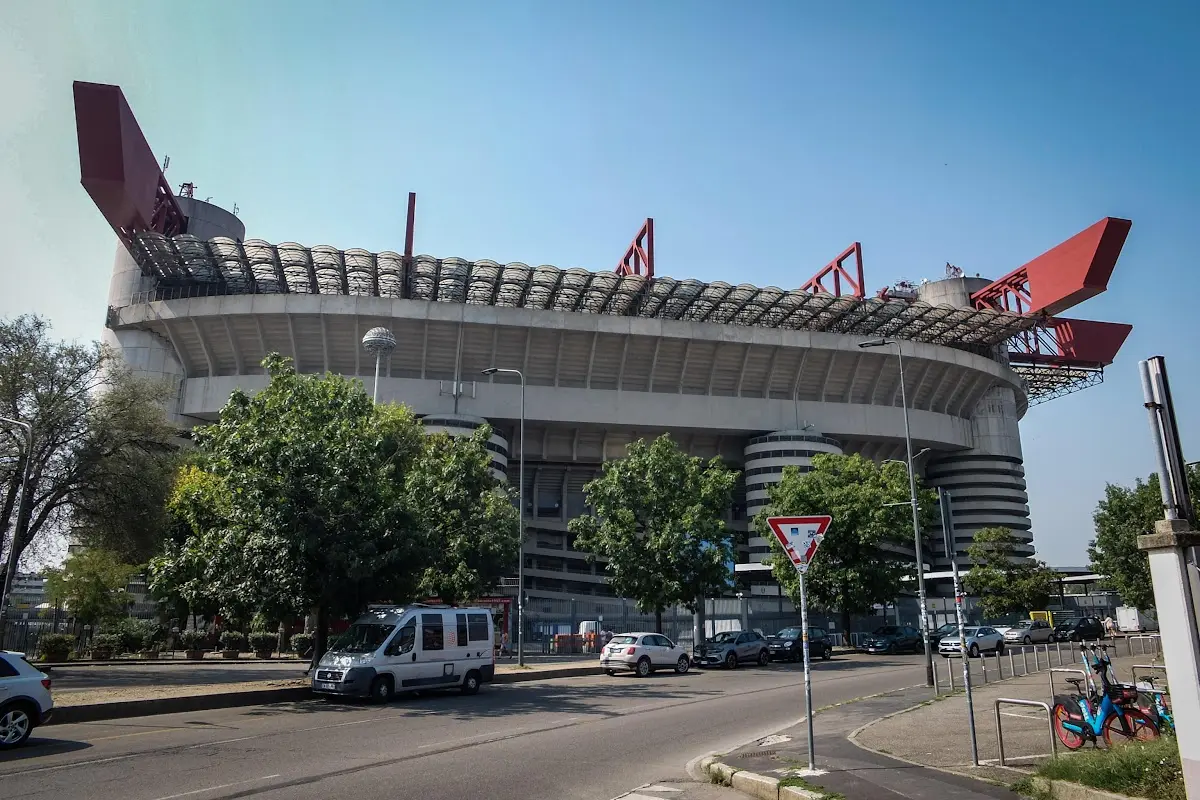 Esterno dello stadio San Siro di Milano con le caratteristiche coperture rosse in primo piano e auto in transito